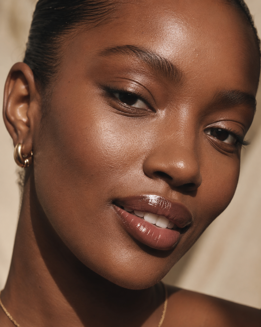 Close editorial portrait with a polished glossy lip finish in warm natural light.