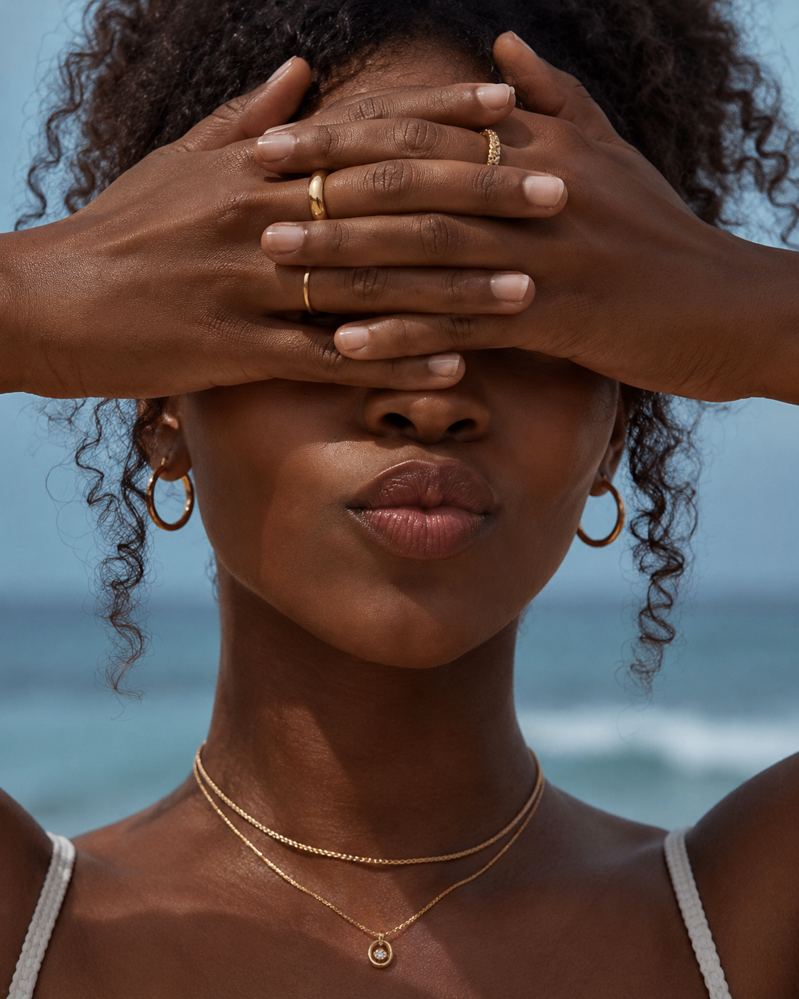 Editorial beach portrait with hands covering the eyes and softly finished lips in focus.