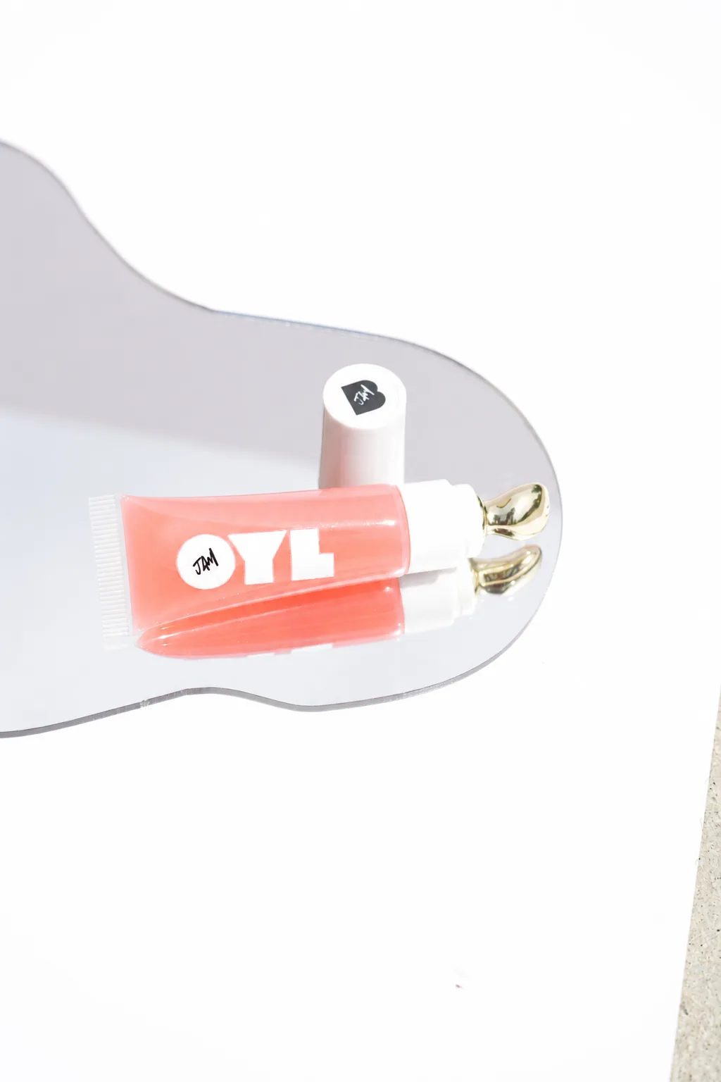 OylJam™ Lip Oil Top Coat in Guava resting on a mirror with a gold applicator detail.