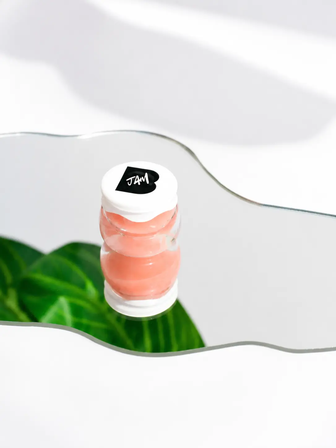 ButtahJam™ Whipped Lip Butter in Guava reflected on a mirror, showing the soft pink jar in editorial light.